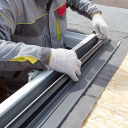 Concept of house under construction. Cropped view of professional worker man checking sealing rubber at new window frame for mansard room, working at wooden rooftop