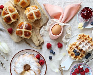 Easter festive dessert table with hot cross buns, cakes, waffles and pancakes. Overhead view