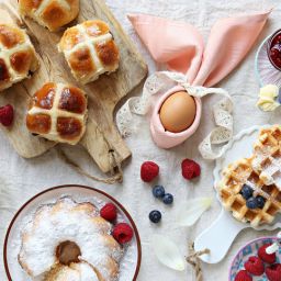 Easter festive dessert table with hot cross buns, cakes, waffles and pancakes. Overhead view
